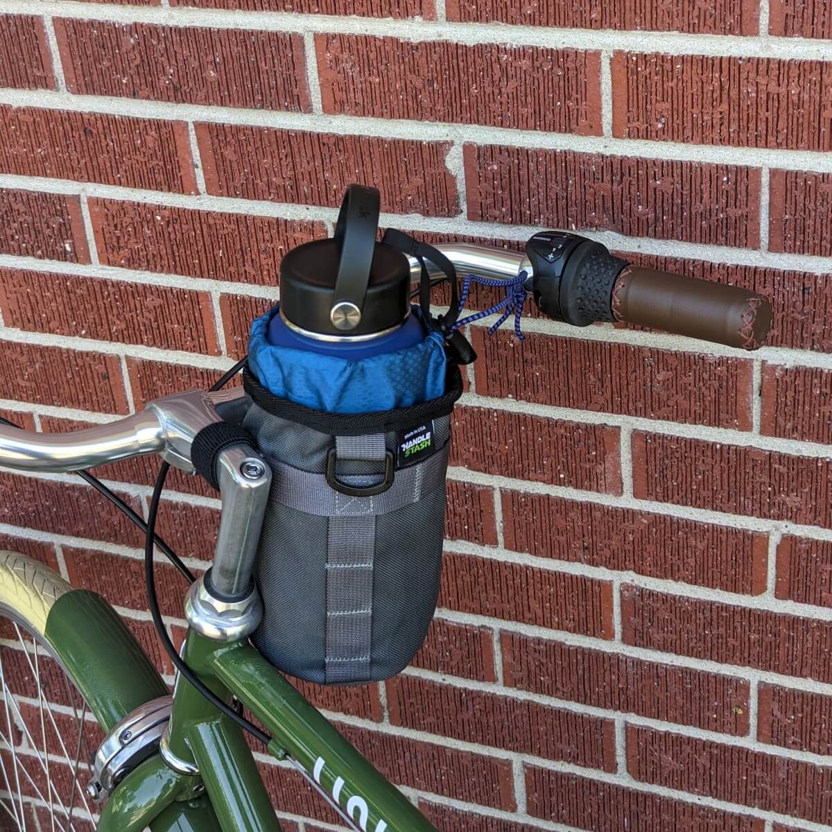 Grey stem bag with navy blue liner on bike holding a large water bottle.